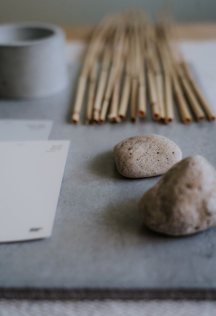 A minimalist still life featuring stones and bamboo sticks on a textured surface, offering a calm aesthetic.